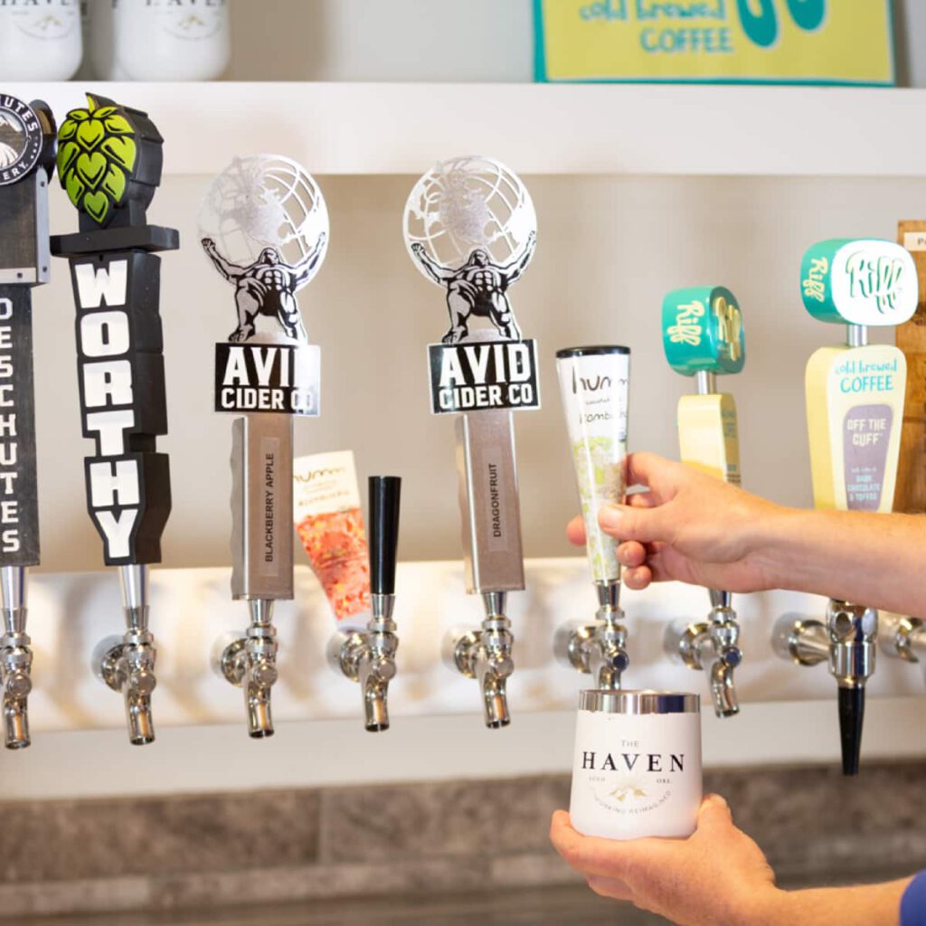 A close-up of the drinks on tap at The Haven, with a person pouring themselves a kombucha from Humm.