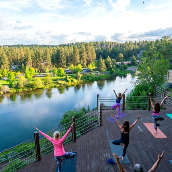 A group of women doing yoga on the deck at The Haven, overlooking the Deschutes River on a clear, beautiful day.