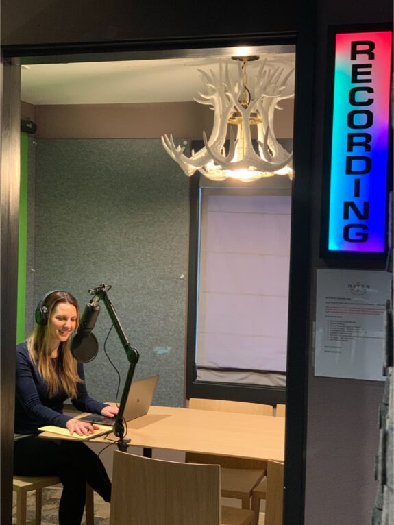 A Haven member smiling at the microphone in the podcast room with the recording sign turned on.