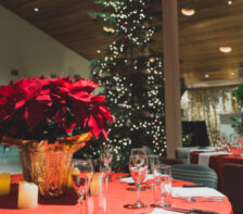 An evening shot of a beautifully decorated table at a holiday event at The Haven, with red flowers and a Christmas tree lighted in the background.