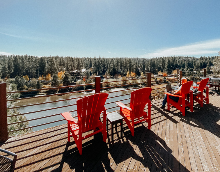 Four red chairs line the deck at the haven coworking, overlooking the deschutes river and pine trees.