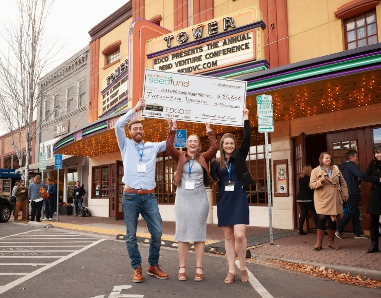three people hold up a big check in front of the tower theater in downtown bend oregon