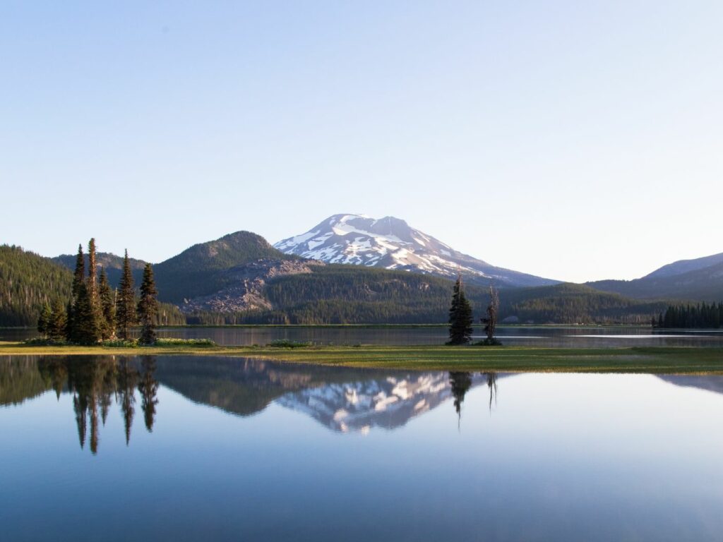 view of mountain in central oregon reflecting on the lake with pine trees lining the background