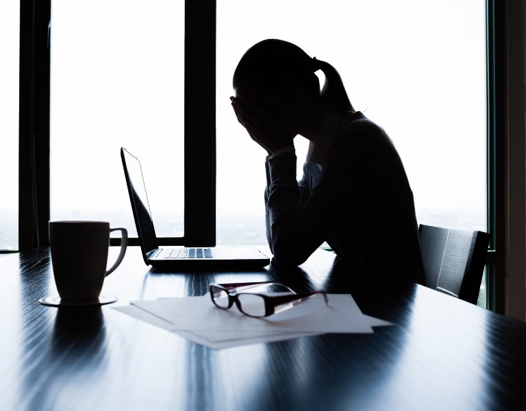 silhouette of a woman slumped over her desk as she experiences the stages of burnout.