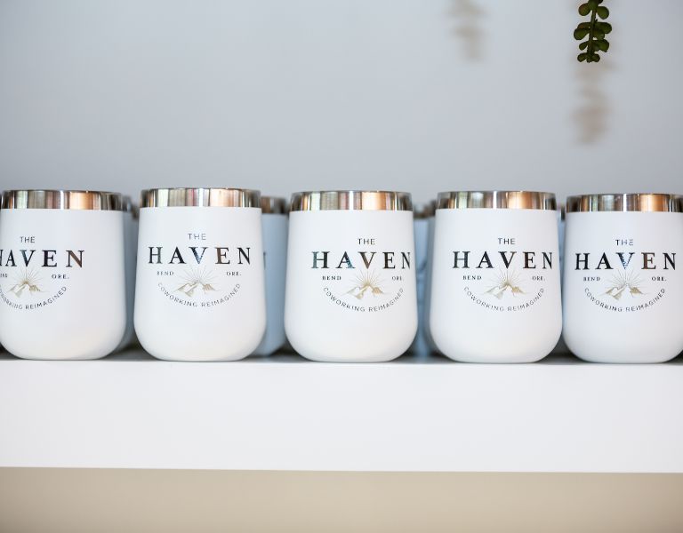 white reusable mugs with haven logo that contribute to environmental benefits of remote working